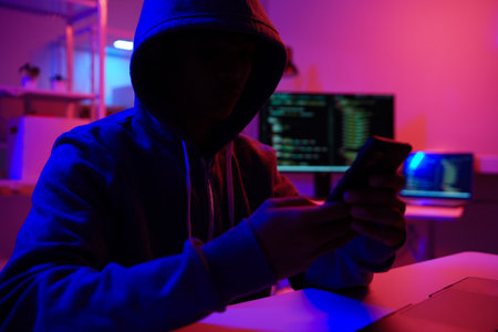 A mysterious hooded hacker working on a computer in a dark room.の写真素材