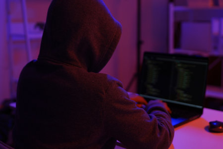 A mysterious hooded hacker working on a computer in a dark room.の写真素材
