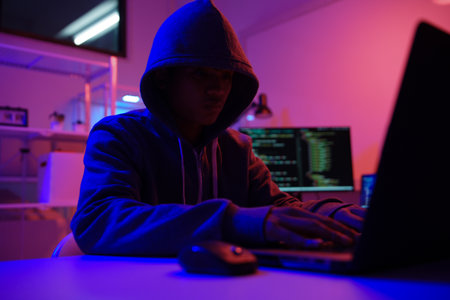 A mysterious hooded hacker working on a computer in a dark room.の写真素材