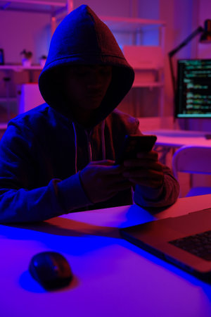 A mysterious hooded person working on a computer in a dark room.の写真素材