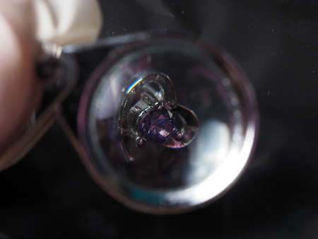 Close up shoot of silver earring with faceted amethyst gem. Shot on black background.