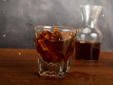A cup of iced coffee on a wooden table with a jar container. Shoot on dark mood styleの写真素材