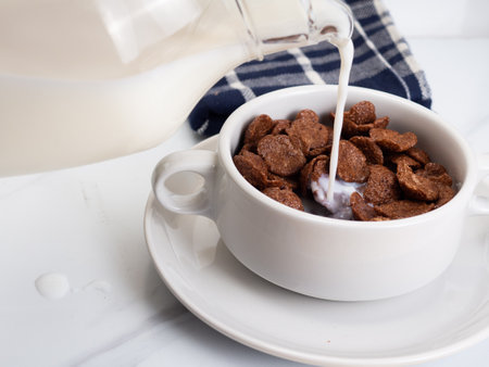 Chocolate cereal with milk on a white bowl, placed on a white marble table
