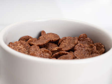 Chocolate cereal with milk on a white bowl, placed on a white marble table