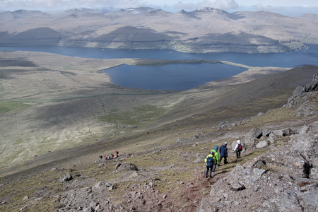 Horizontal scenery image of Faroese landscape with beautiful mountains and the North Atlantic Ocean in distant background and group of unidentifiable young people on their hiking trail walking down the way. Glorious sceneries of the Faroes. Postcard motif.の写真素材