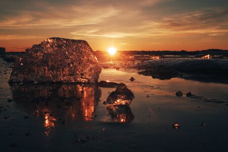 Pieces of beautiful transparent ice in pink and amber colors as a jewels shining on a frozen seashore in the sunsetの写真素材