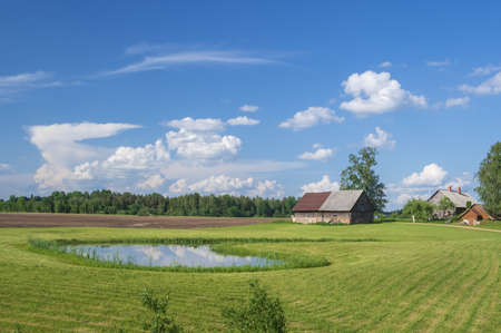 Rural landscape with green and brown fields, blue pond in the middle and beautiful white clouds in...