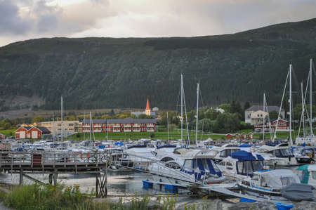 Nesna, Nordland/Norway - August 9 2016: View to the boats in Nesna port, Norway, with Nesna town in the background in sunset light, in cloudy summer eveningのeditorial素材