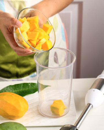 Asian Female Making Mango Juice with Hand Blender. Step by Step, Put Mango Dice on Blender Bowlの写真素材