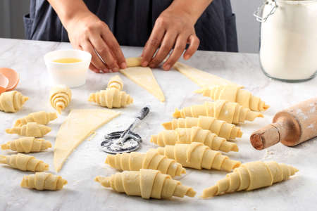 Producing classic croissants at the bakery shop. Woman is rolling dough into rolls for further...