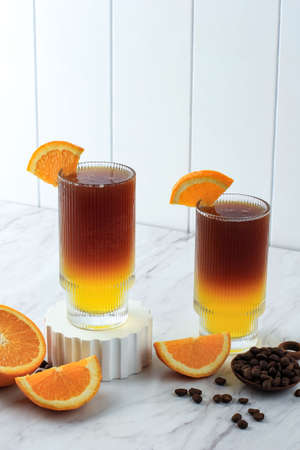 Iced Americano Black Coffee and Layer of Orange and Lemon Juice Decorated with Sliced Orange and Coffee Bean on Marble White Backgroundの写真素材