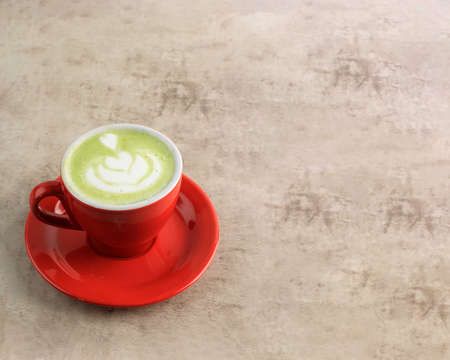 Matcha Green Tea Latte on Red Cup Above Marble Brown Background