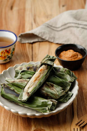 Otak-otak Tengiri with Peanut Sauce, Made from fish and flour Wrap with Banana Leaves, on Wooden Tableの写真素材