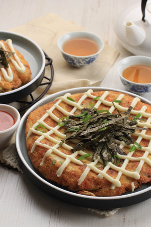 Homemade Okonomiyaki. Osaka flour dish with mayonnaise, spring onion, and sauce. Served on Ceramic Plate with Teaの写真素材