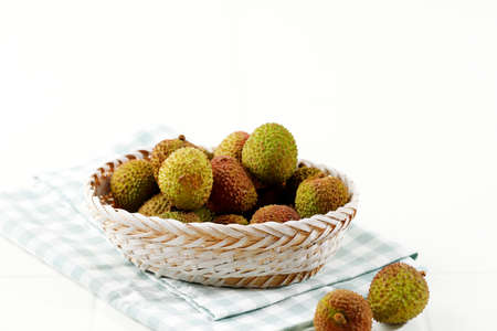Green Lychee Fruit on Rattan Basket, Isolated on White Table. with Checkered Napkin. Copy Space for...