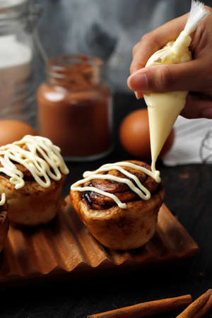 Hand of Female Chef Topping Cream Cheese Sauce  the Top  Fresh Delicious Cinnamon Rolls, Baking Process in the Kitchenの写真素材