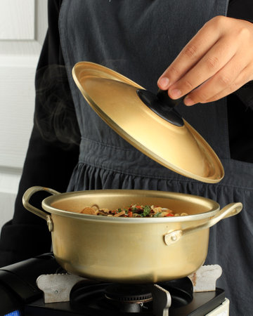 Cooking Ramyeon Korean Instant Noodle on the Stove, Female Hand Open Golden Pot Lid