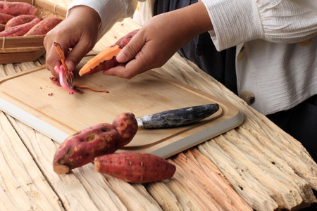 Peeled Red Sweet Potato, Female Hand Hold Peeler Knife on Wooden Tableの写真素材