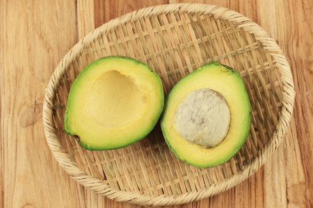 Slice Avocado on Rattan Plate, Above Wooden Tableの写真素材