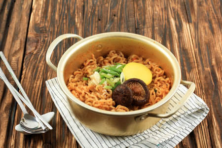 Close Up Korean Style Instant Noodle, Ramyeon or Ramyun with Spicy Flavour topped with Mushroom, Spring Onion, Sesame Seed, and Danmuji. Served in Traditional Korean Noodle Pot.の写真素材