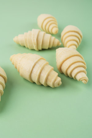Raw Croissanr Layered of a Fluffy Leavened Uncooked Traditional French Croissants Dough Roll, on Mint Green Backgroundの写真素材