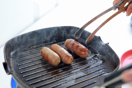 Cooking Process Making Grilled Sausages in the Kitchen, Smoke from the Grillingの写真素材