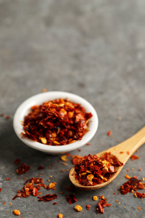 Red Chilli Flakes on Wooden Spoon above Dark Backgroundの写真素材