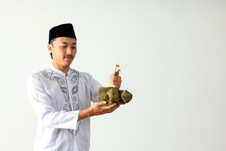 Muslim Asian Man Wearing  White Shirt Baju Koko  and Black Caps Kopyah Holding Ketupat Rice Cakes for Eid al Fitr. Copy Space for Textの写真素材