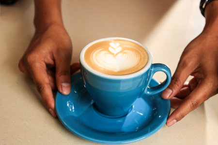 Barista Hand Holding Blue Cup with of Coffee Latte with  Latte Art Serving to Customer