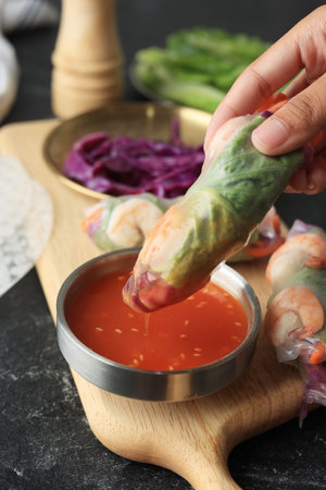 Female Hand Dipping Vietnam Fresh Vegetable Spring ROll to the Sweet and Sour Sauce with Sesame Seed
