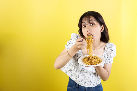 Happy Asian Woman Eating Noodles, Wide Open Mouth. Isolated on Yellow Backgroundの写真素材