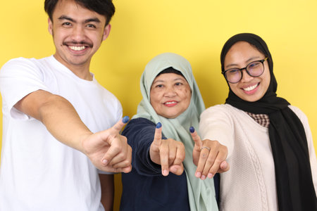 Three People Indonesian Family Showed Tinta Pemilu, Inked Finger after Voting for General Election or Pilkada, on Yellow Backgroundの写真素材