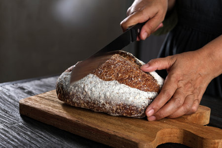 Female Hand with Sharp Knife Slicing Cut Rustic Sourdough Breadの写真素材