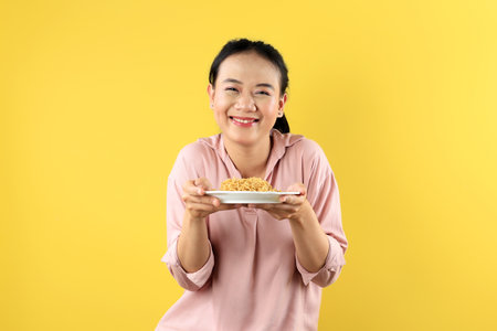 Young Indonesian Woman Happy Holding Mie Goreng Instant Noodle On White Plate, Isolated on Yellow Backgroundの写真素材