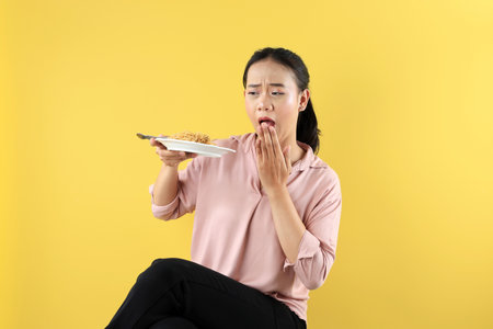 Asian Young Woman Sitting and Holds a Plate of Noodles in one Hand While Gesturing Excitement with the other Hand Near Her Mouth. Makanan Pedas or Hot Spicy Food Concept.の写真素材
