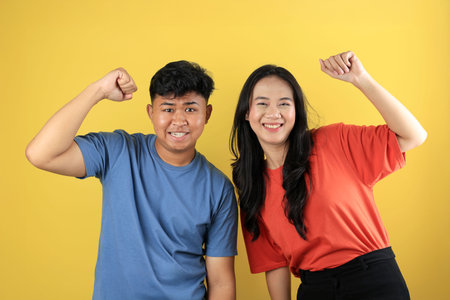 Young Asian Couple using Casual Shirt Happy While Clenching Hand On Yellow Backgroundの写真素材
