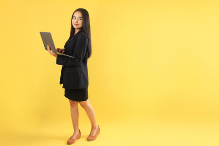 Happy Young Asian Indonesian Businesswoman using Laptop Computer Isolated on Yellow Background, Copy Space for Textの写真素材
