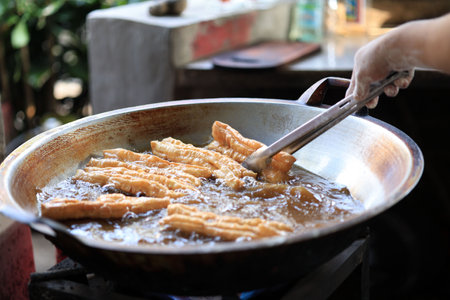 Man Hand Fried Chinese Deep Fried Dough Stick or Youtiao in Big Pan with Hot Oil. Known as Indonesian Street Food Cakue or Cakwe.の写真素材