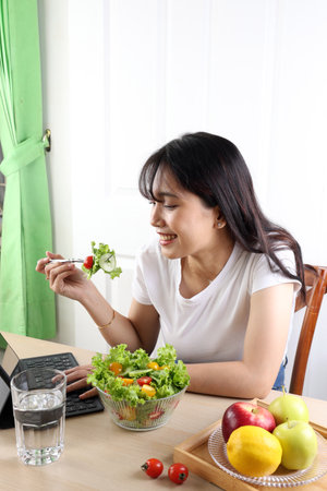 South East Asian Beauty Woman Eating Green Healthy Salad While Watching FIlm on Tablet Computer