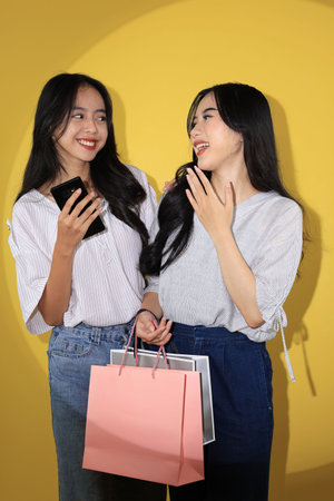 Happy Two Shopaholic Asian Woman Friends Smiling After Shopping with Various Color Paper Bagsの写真素材