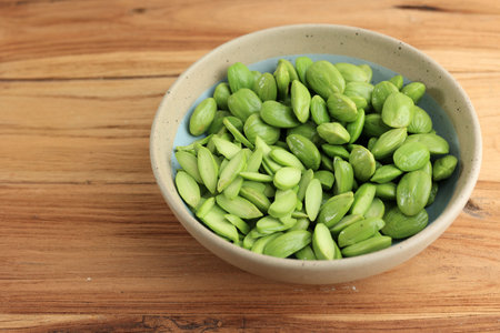Sliced Petai Kupas Raw Green Bean on Ceramic Bowl above Wooden Tableの写真素材
