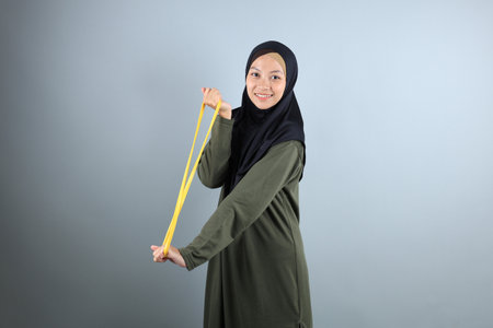 Young Asian Hijab Woman Stretch Yellow Resistance Band for Hand Pilates Exercise before Workout,...