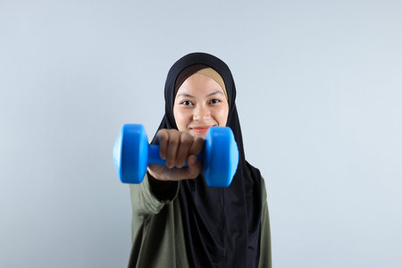Sporty Muslim Indonesian Woman training with Blue Dumbbells, Isolated on Grey Backgroundの写真素材