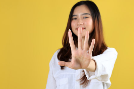 Smiling Blond Young Woman Extend Hand To Show Stop Sign, Rejecting Something with Unbothered Happy Face Expression, On Yellow backgroundの写真素材