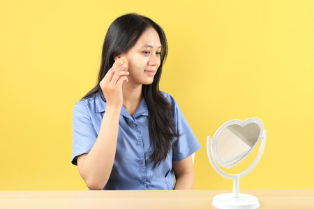 Young Asian Beautiful Girl Applying Foundation or CC Cream using Beauty Blender While Looking at the Mirror, Make Up Step by Step.の写真素材
