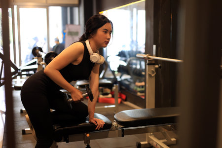 Young Female Training at the Gym Using Dumbbells While Listening to the Musicの写真素材