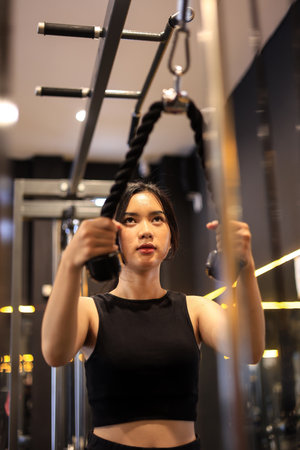 Young Woman doing Cable Arm Exercises at the Gym, using the Rope Attachment for Triceps Push Down.の写真素材