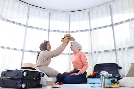 Two Young Asian Friend Preparing Travelling, Trying on a Hat on Her Friend to See Which Outfit  Matchの写真素材