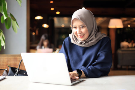 Middle Age Muslim Asian Women with Hijab Working at a Cafe and using Laptop Computer.