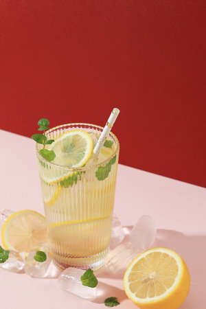 Refreshing Drink with Ice, Lemon, and Mint. Cold Lemonade on Pink Red Backgroundの写真素材